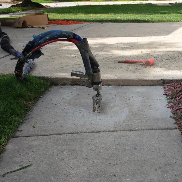 Concrete slab lifting equipment injecting material beneath a sidewalk to raise and level a sunken concrete slab in Lansdowne, VA.